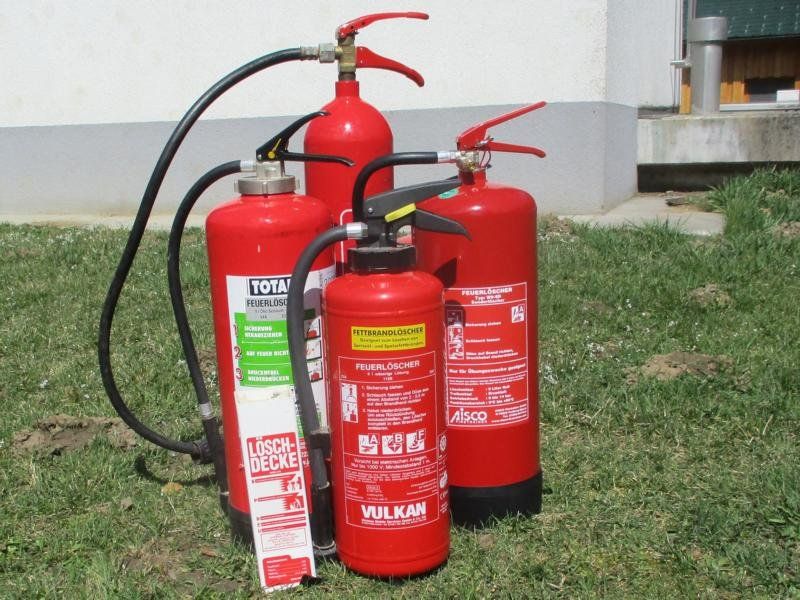 Vier rote Feuerlöscher auf grünem Gras.