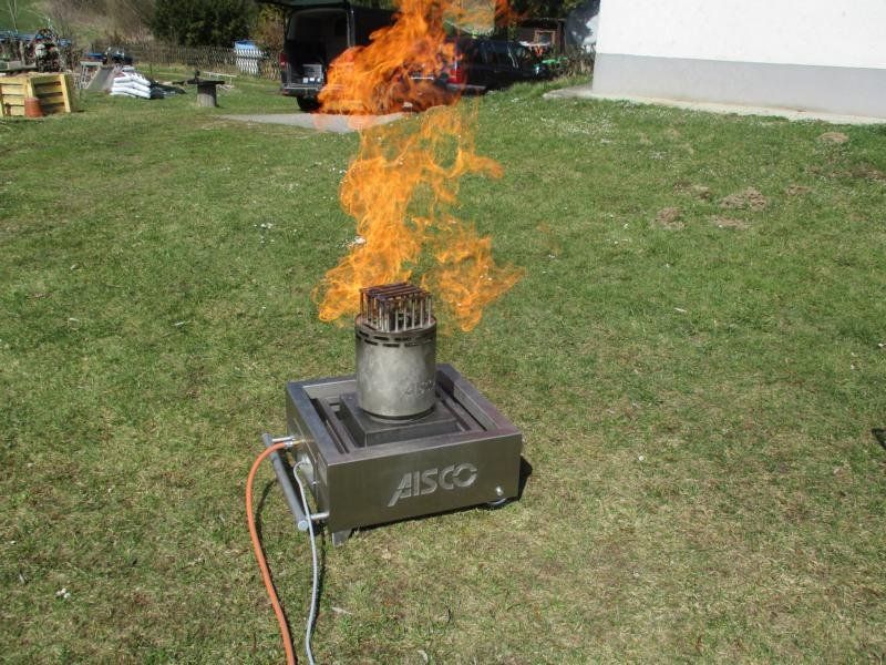 Ein brennender Brennstoffbehälter auf einem Metallsockel, dessen Flammen hoch über einer Rasenfläche schlagen.