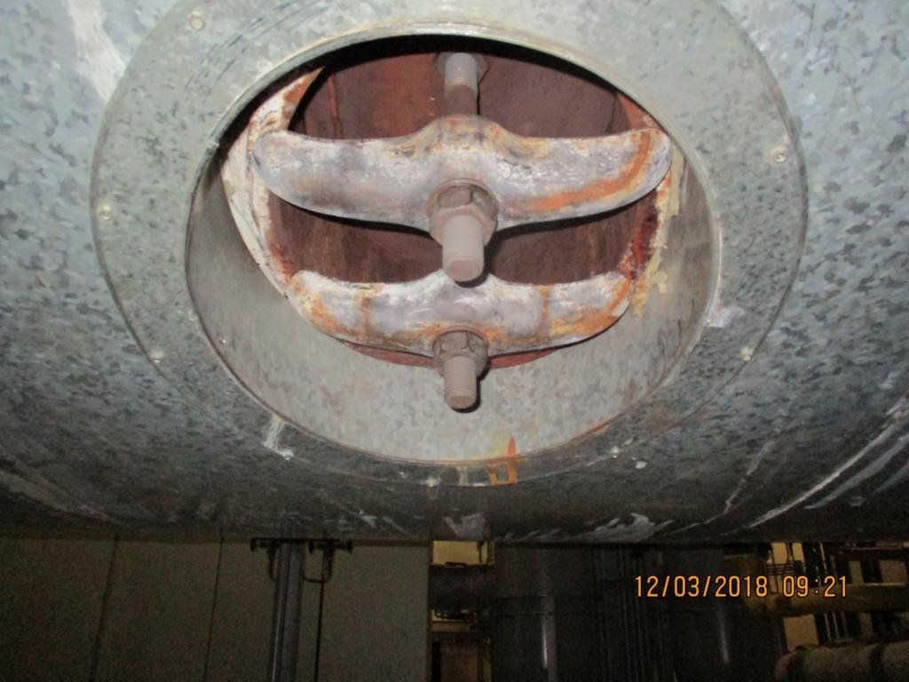 Innenansicht eines industriellen Luftkanals mit verrosteten, gebogenen Metallträgern und einer kreisrunden Öffnung.