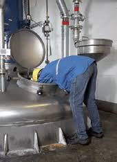 Eine Person in Jeans und Jacke beugt sich in einen offenen Industrietank und überprüft das Innere.