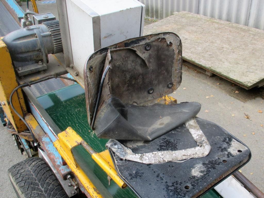 Ein zerrissener, schwarzer Bürostuhl auf einem Förderband, möglicherweise zum Recycling.