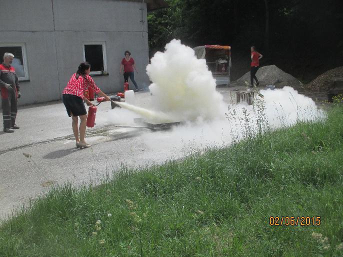 Menschen üben mit einem Schaumlöschschlauch, große Schaumwolke, Betonarbeiten und grünes Gras.