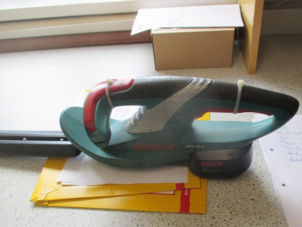 Eine kabellose Heckenschere von Bosch auf einer Theke, im Hintergrund ein gelber Briefumschlag und ein Karton.