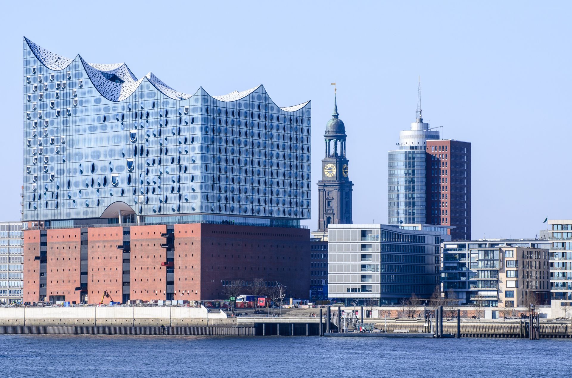 Hamburger Skyline mit Elbphilharmonie und St.-Michael-Kirche, blauer Himmel, Wasser im Vordergrund.