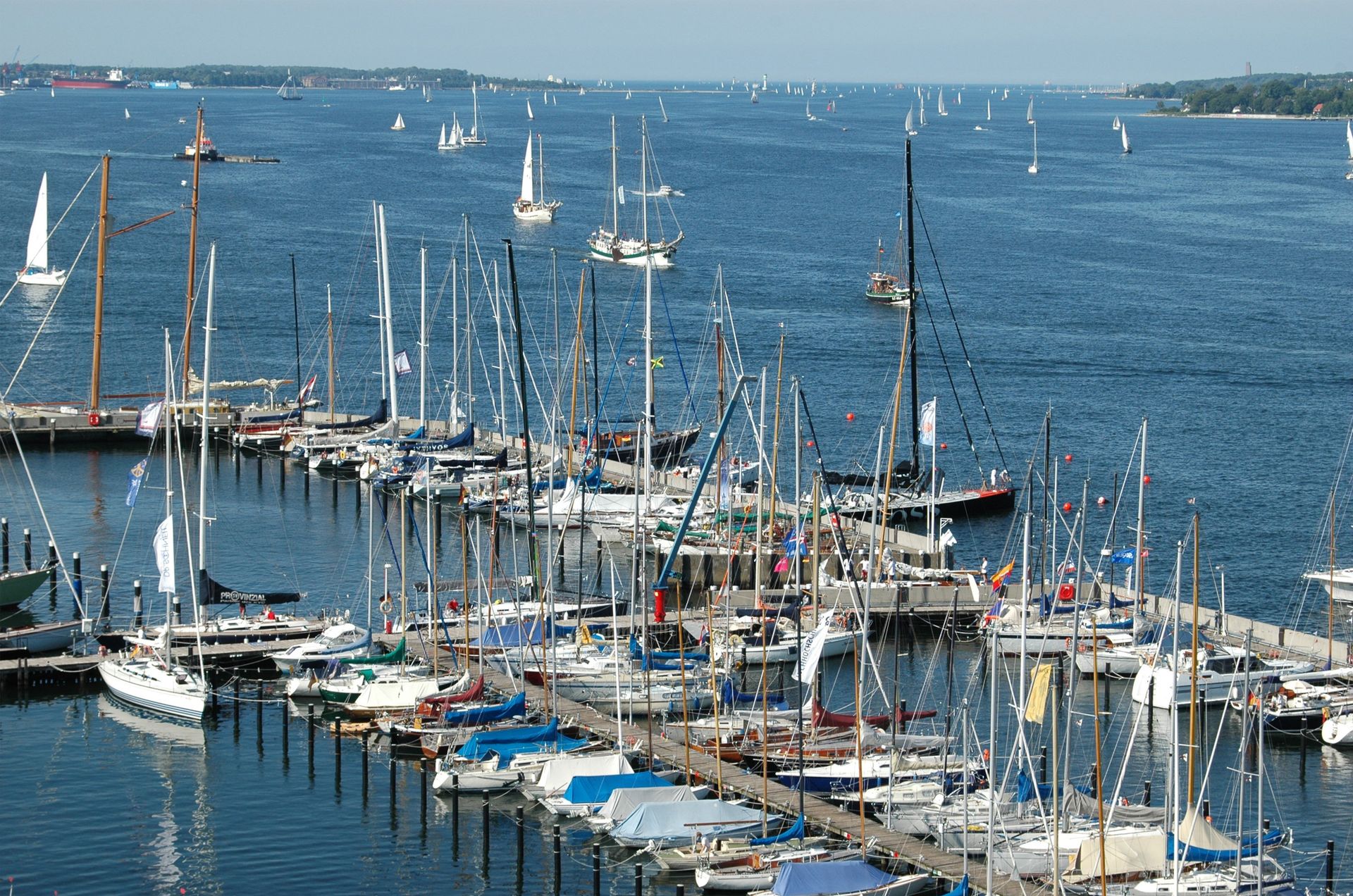 Segelboote lagen in einem Hafen vor Anker, weitere Boote in der Ferne auf blauem Meer unter sonnigem Himmel.