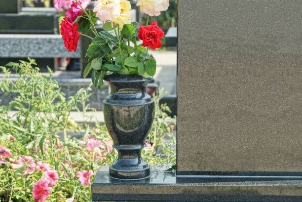 A vase filled with flowers is on a grave in a cemetery.