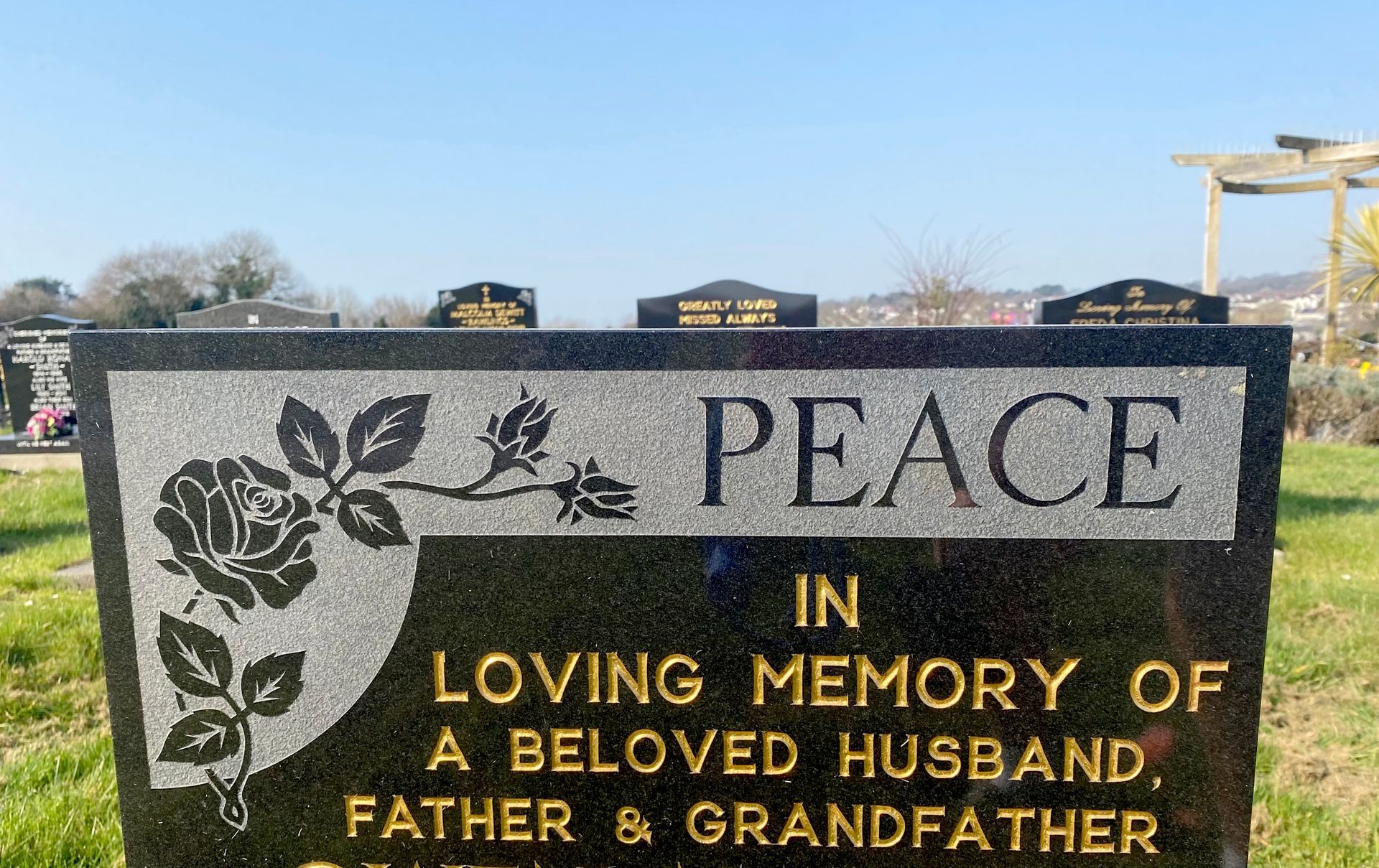 A gravestone in a cemetery that says peace in loving memory of a beloved husband , father and grandfather.