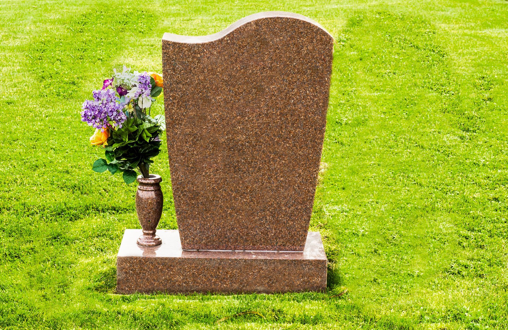 A gravestone with a vase of flowers next to it in a cemetery.