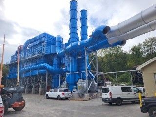 Blue industrial building with cylindrical tubes extending outward, vehicles in foreground.