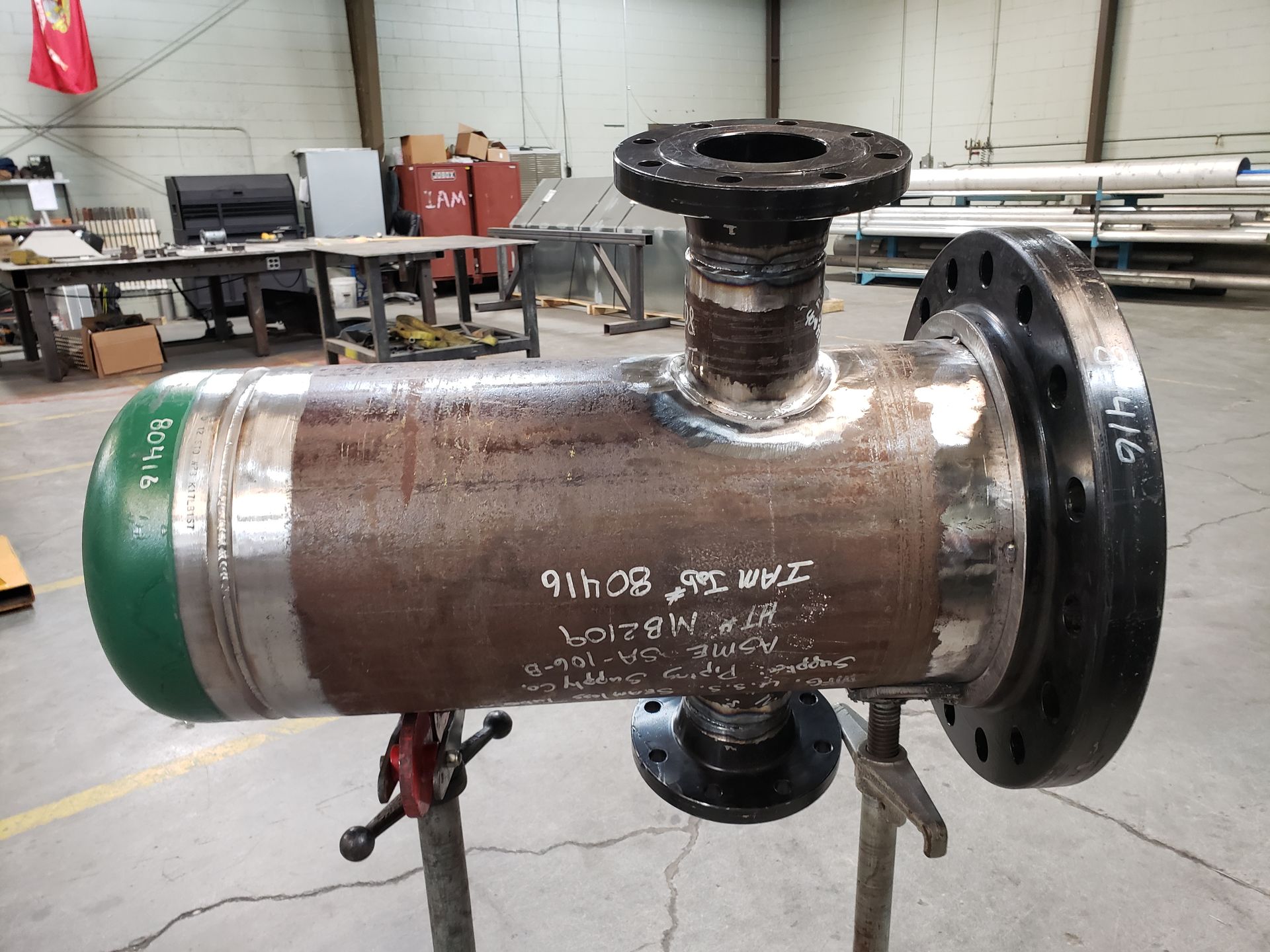 Welded metal industrial component with flanges and a green cap. It rests on supports in a workshop.