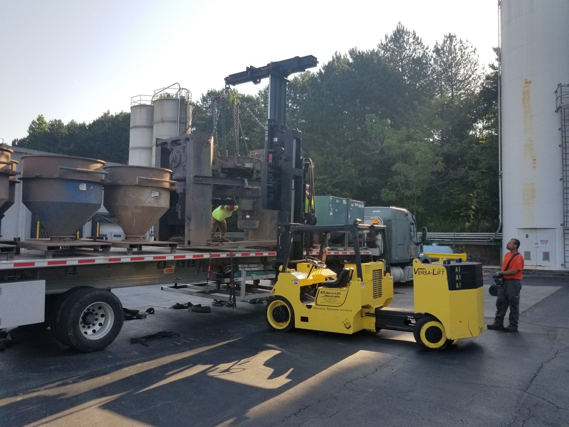 Forklift unloading industrial equipment from a flatbed trailer, outdoor setting.