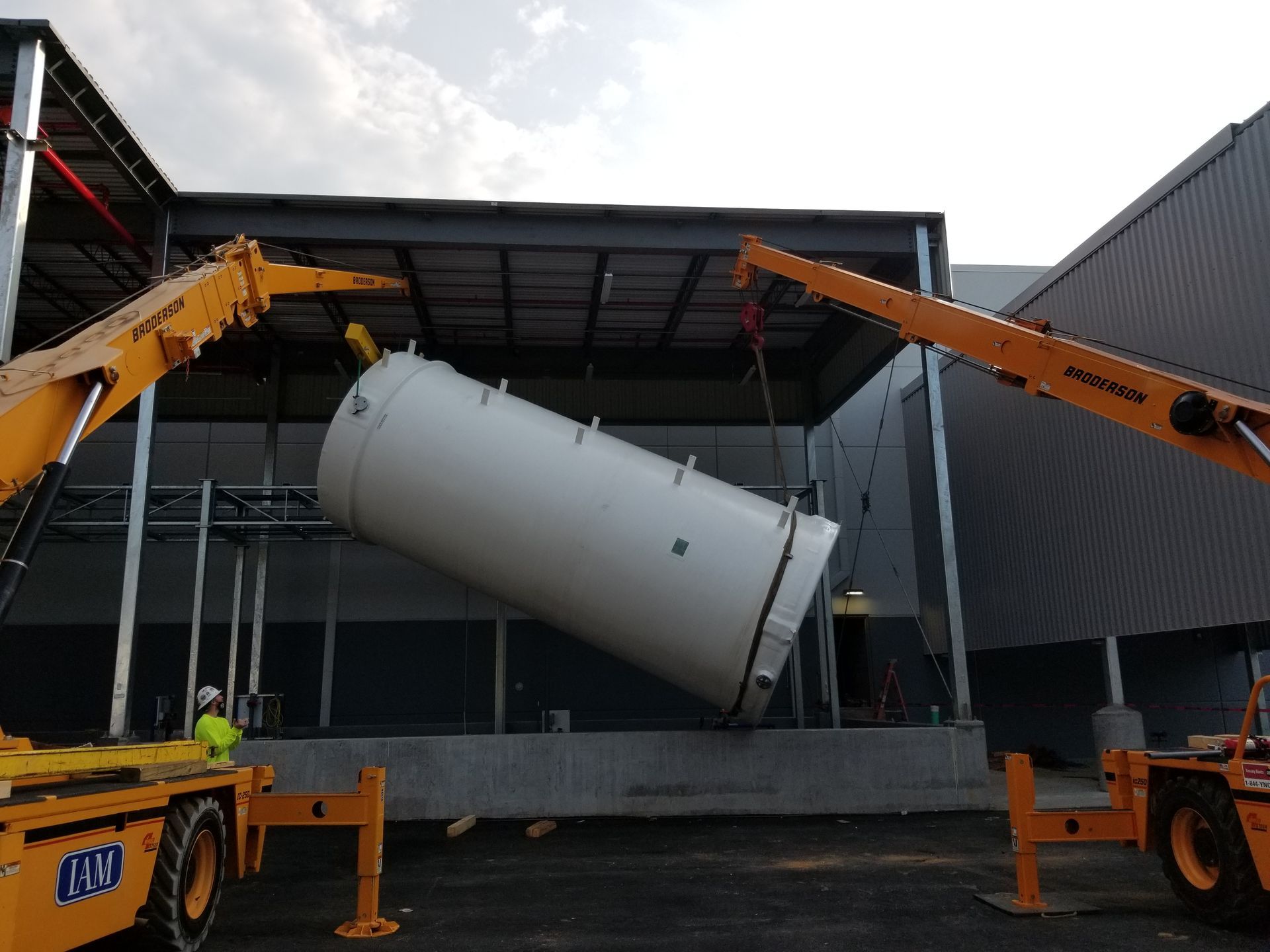 Two cranes lift a large white tank into a building.