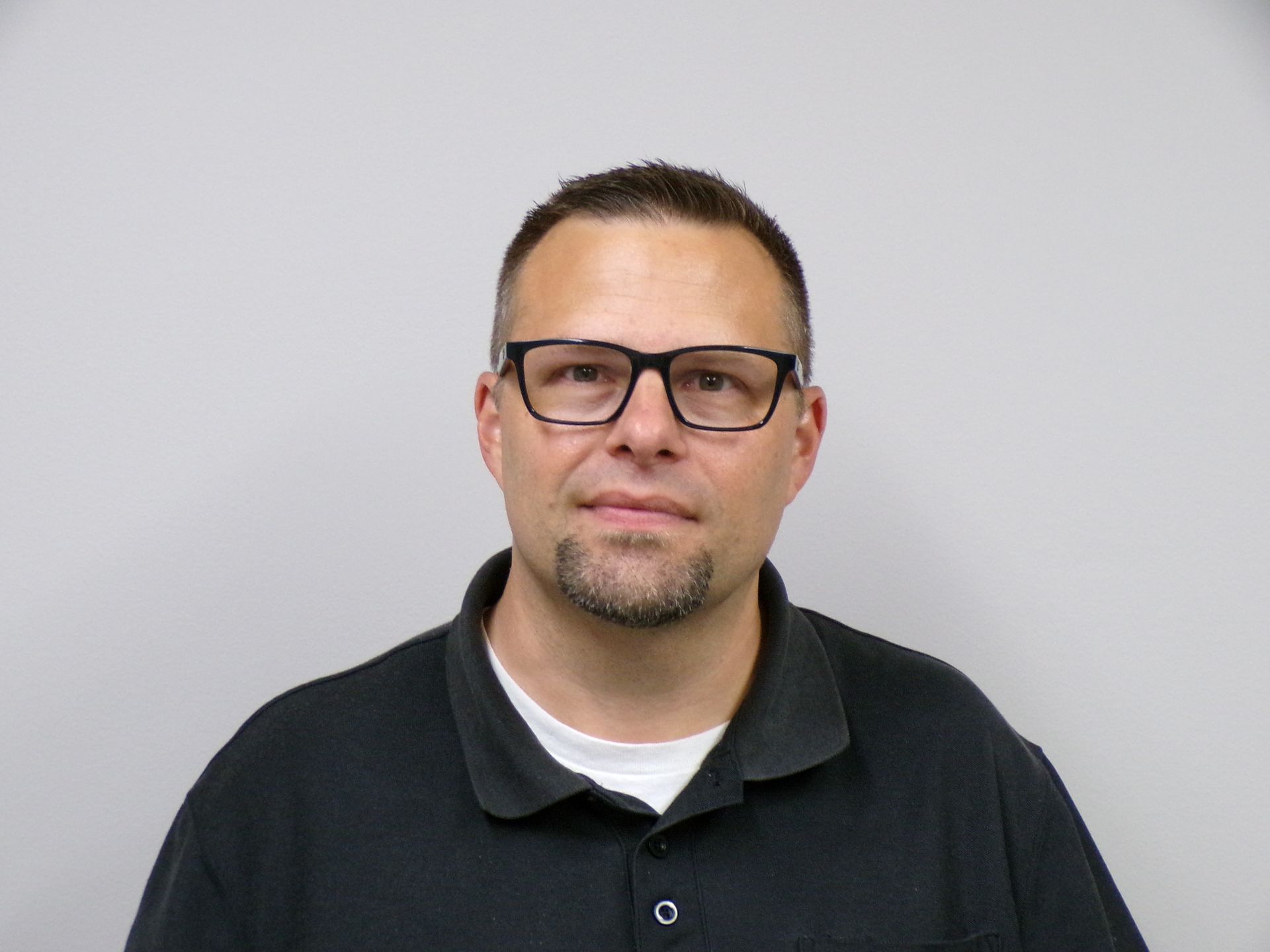 Man with glasses and goatee in a black shirt against a plain background.