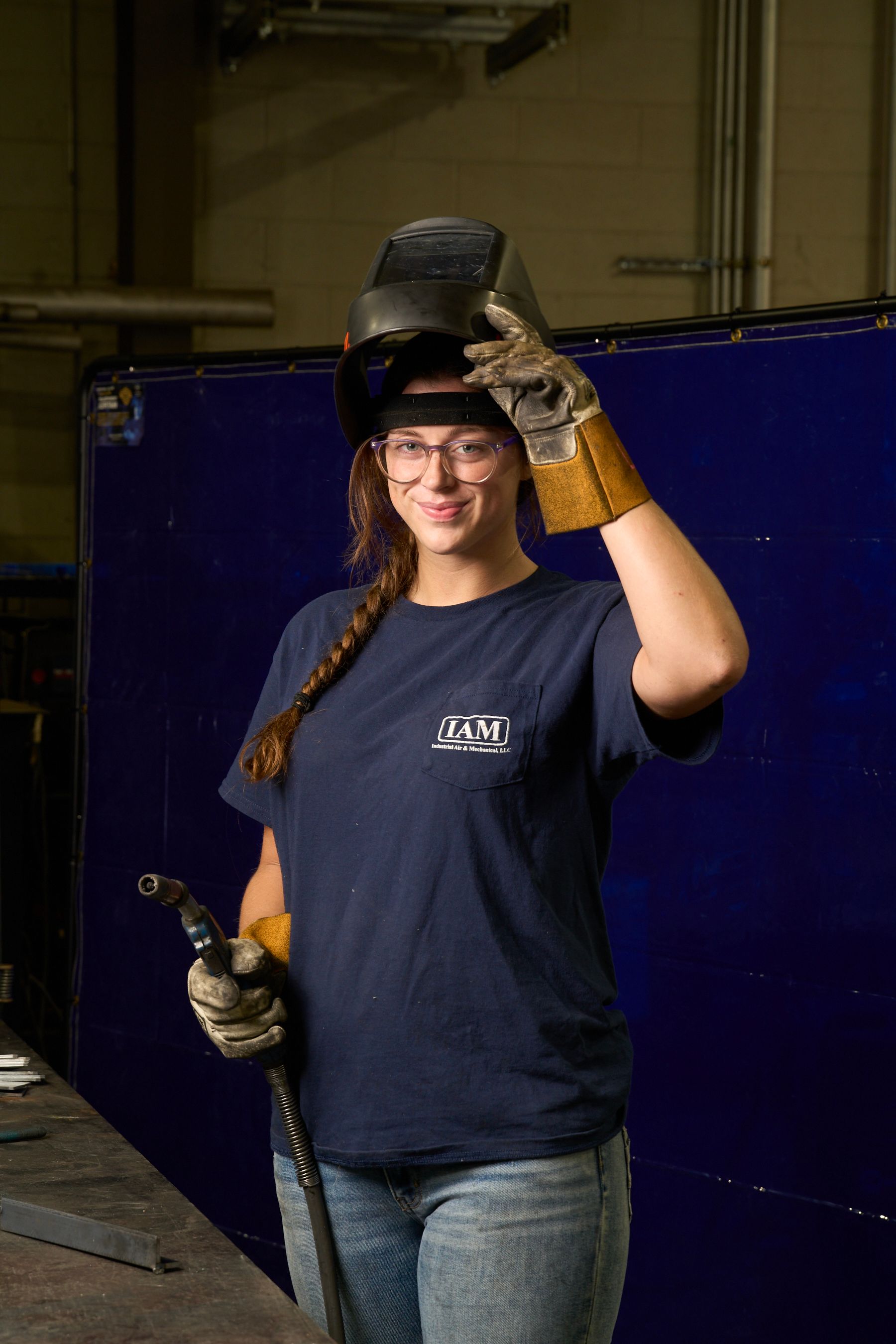 Welder wearing a welding mask and gloves, holding a welding torch in a workshop.