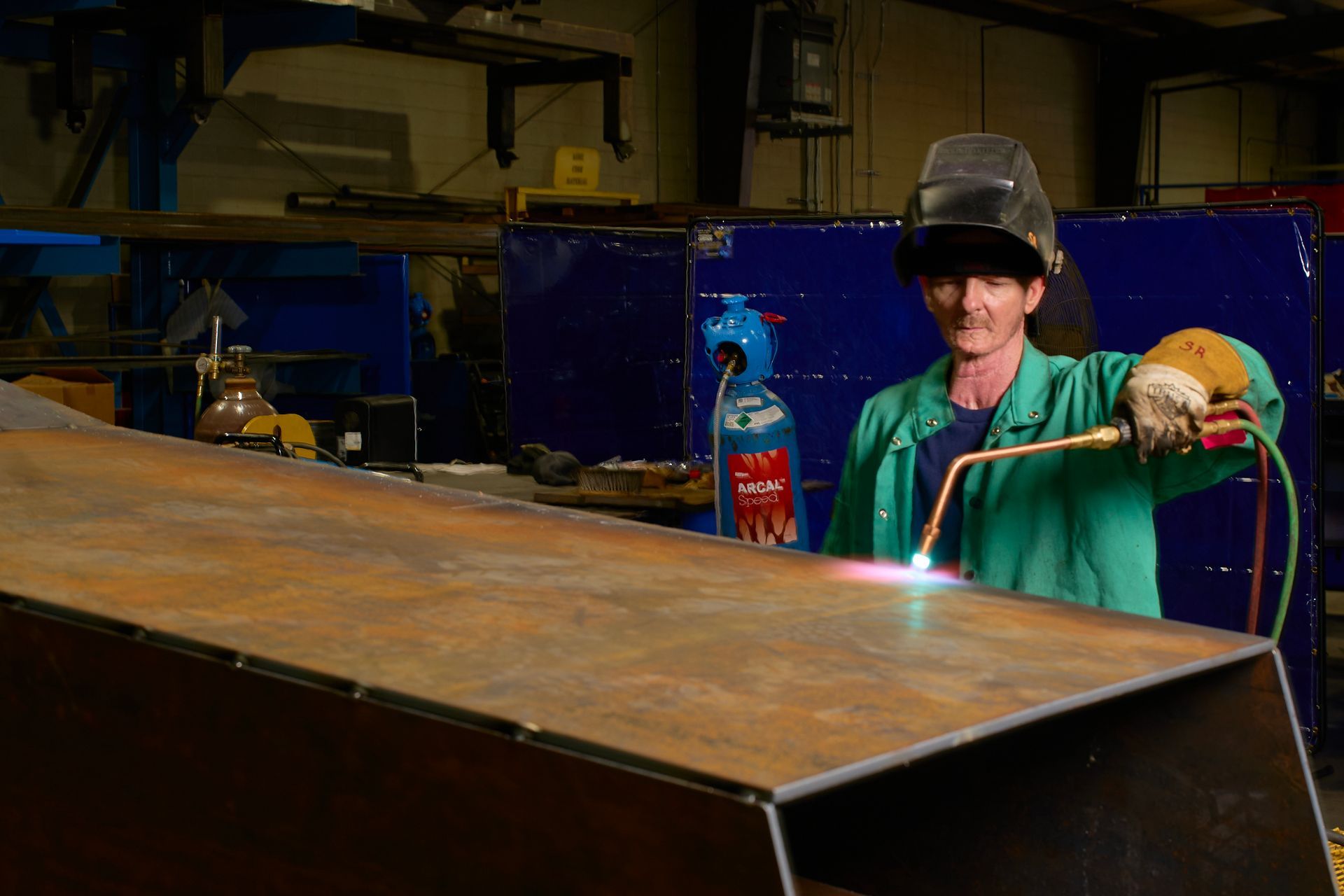 Welder with helmet and torch, cutting metal in a workshop. Sparks fly.