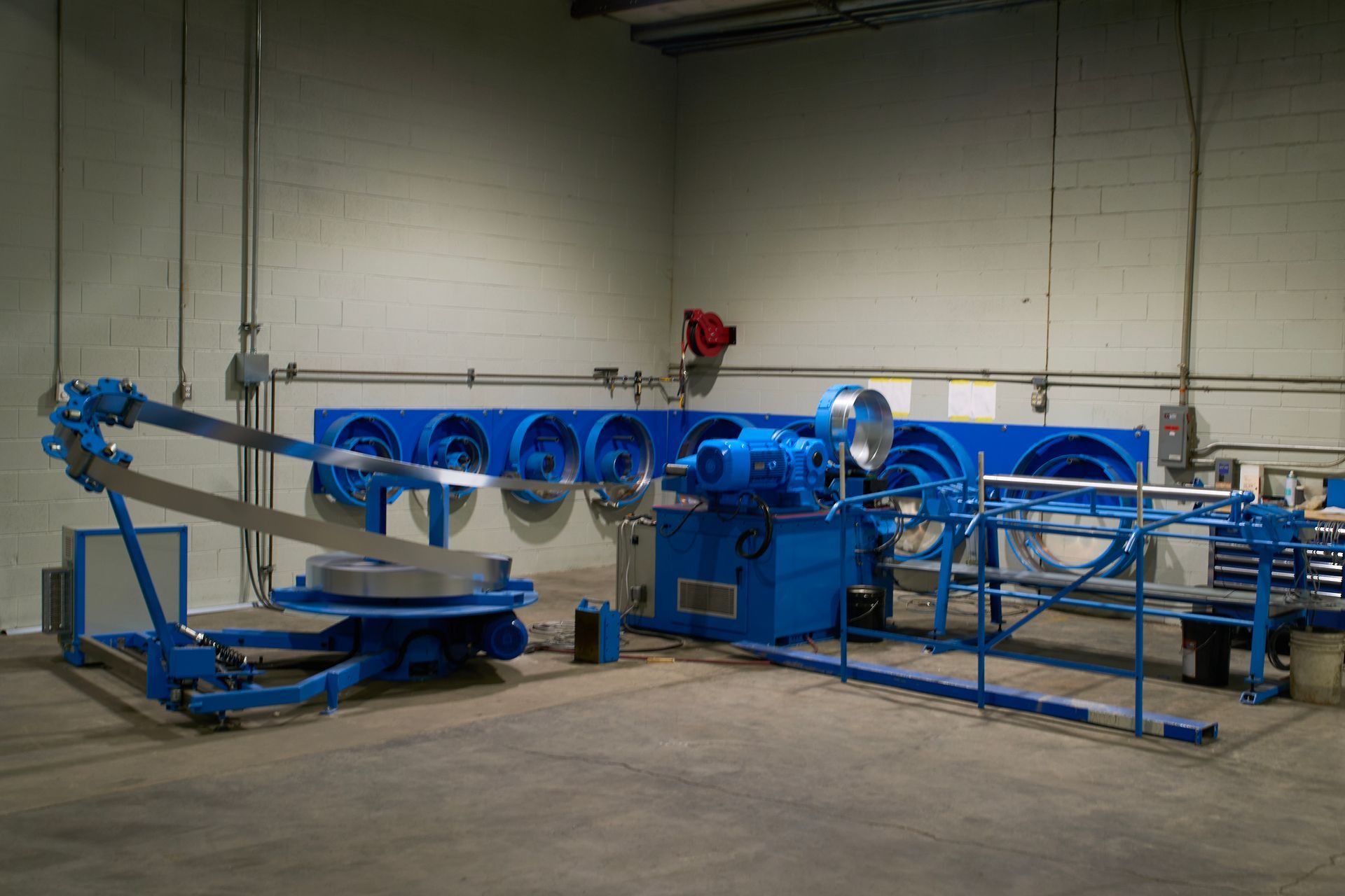 Blue industrial machine in a warehouse setting, with large fans, pipes, and metal components.
