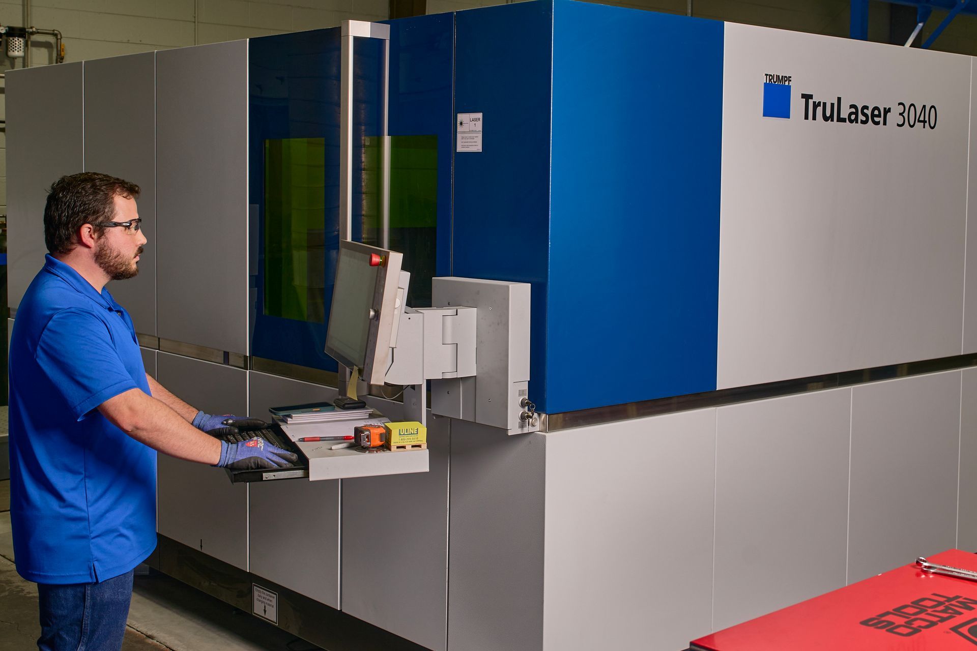 Man operating a TruLaser 3030 laser cutting machine in a factory setting.