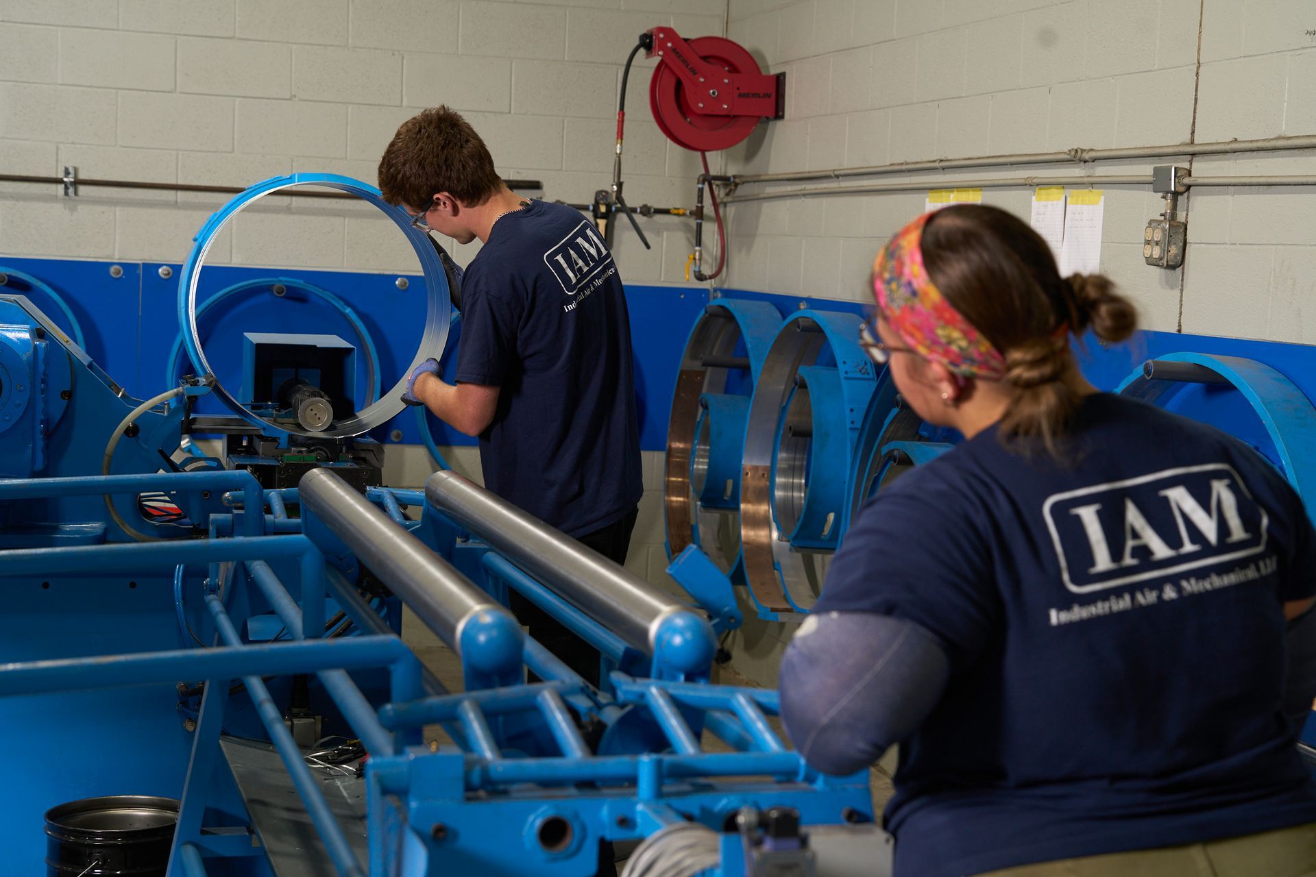Two people in blue shirts work on machinery at a manufacturing facility.