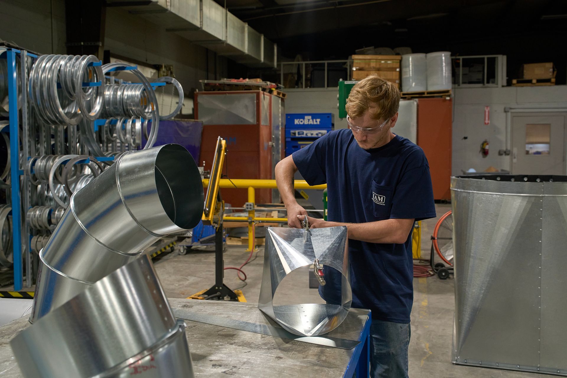 Man working with metal HVAC ductwork in a manufacturing facility.