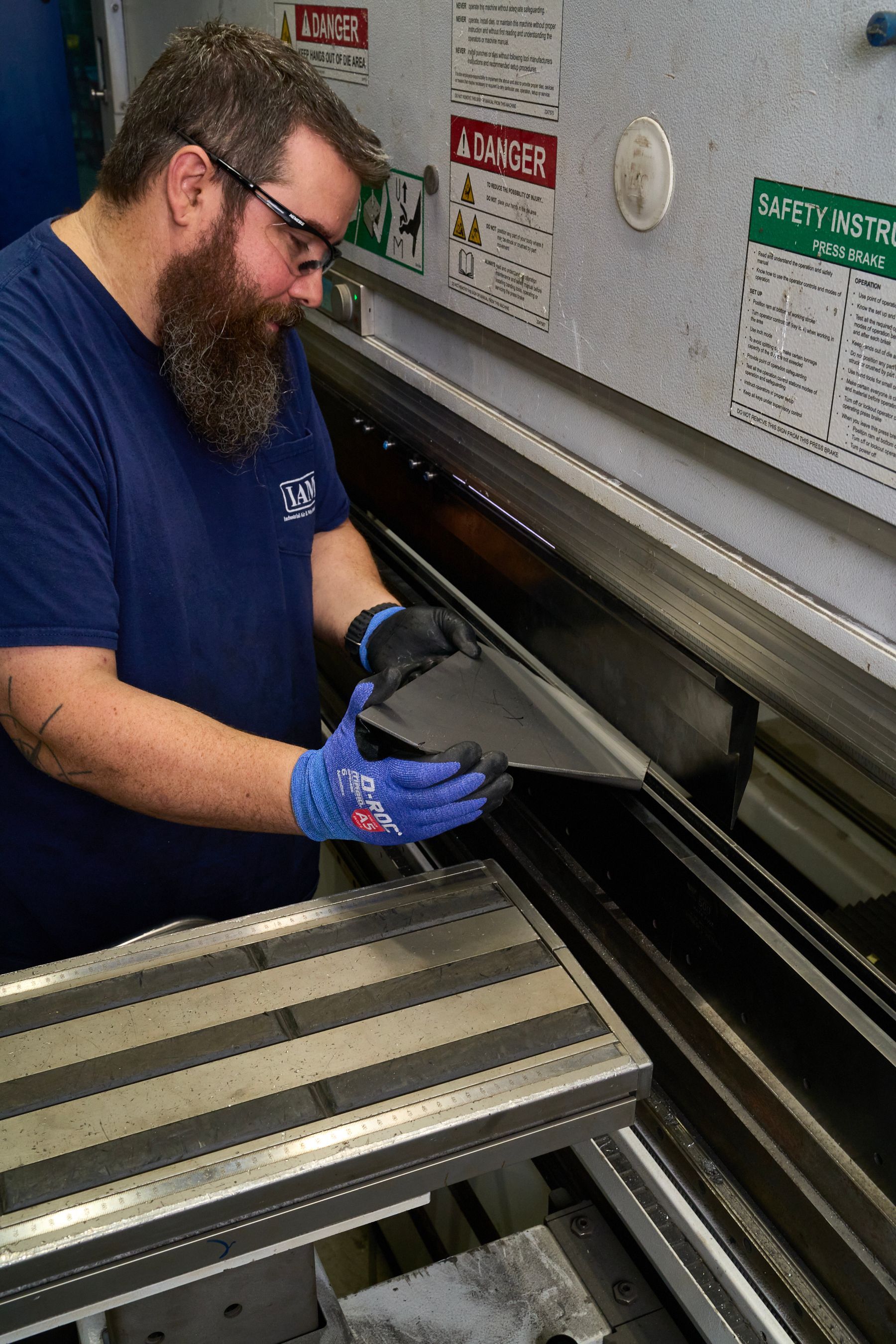 Man in safety glasses and gloves bends metal sheet on industrial machine.