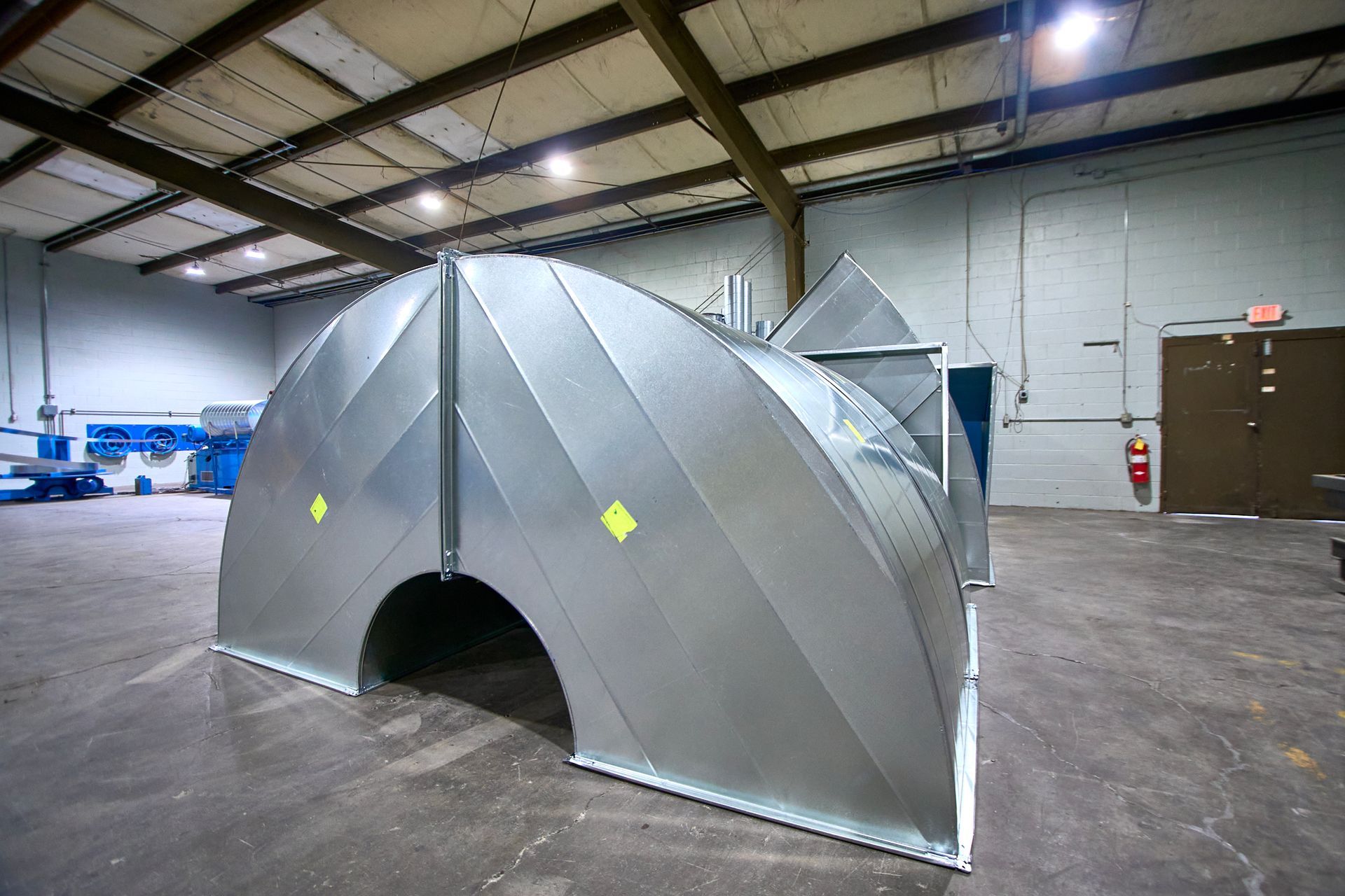 Large, silver-colored metal ductwork in an industrial setting with a concrete floor.