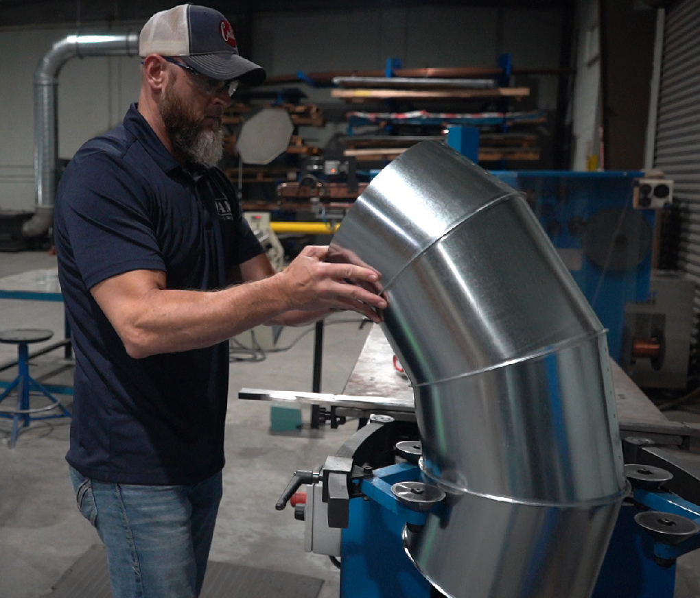 Man in workshop assembling a metal duct elbow.