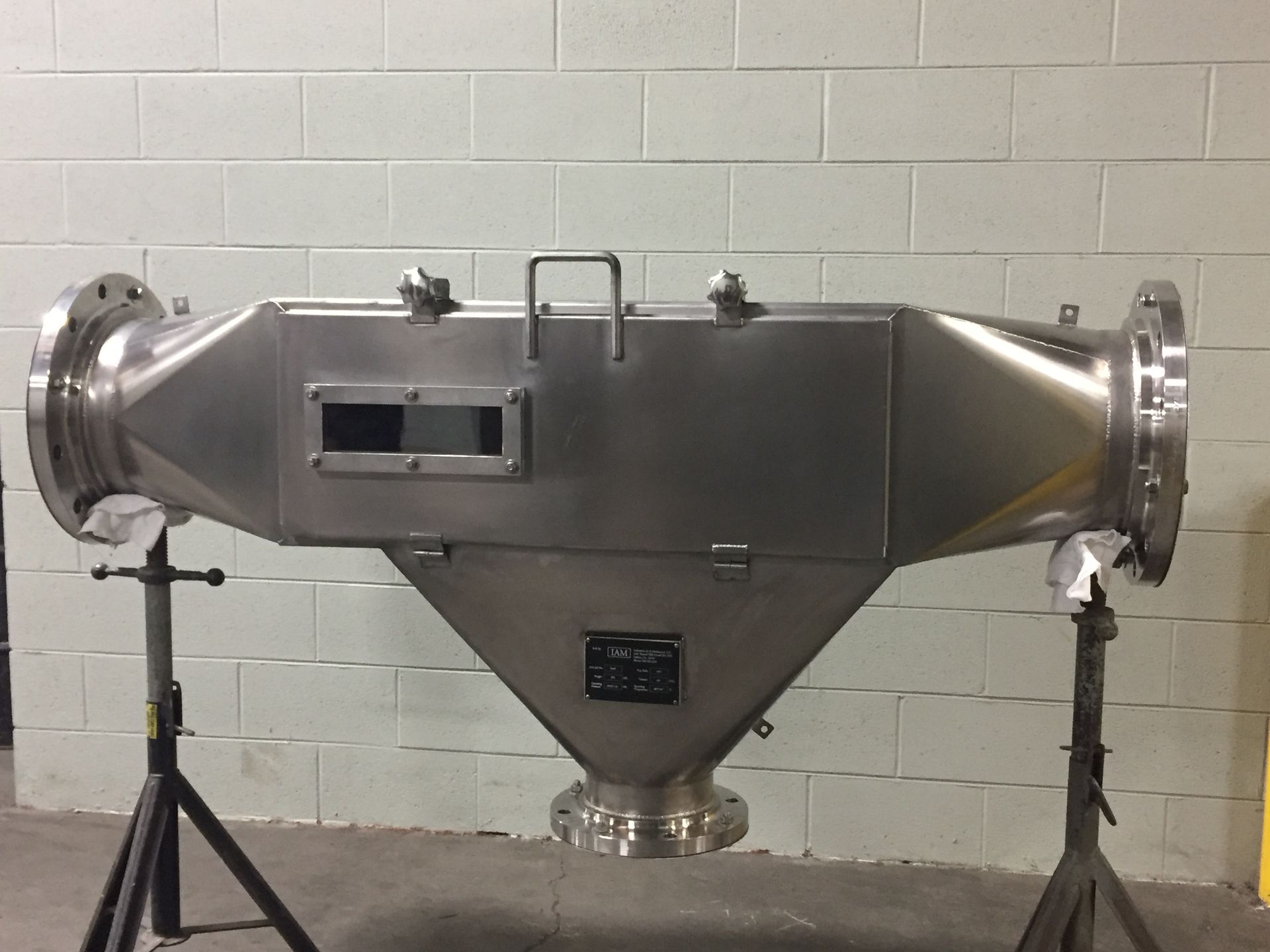 Stainless steel industrial metal detector with flanges, resting on support stands.