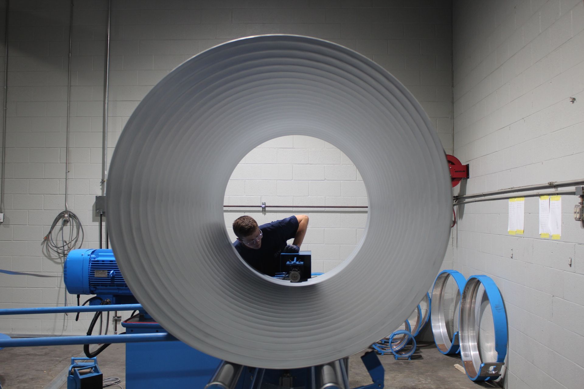 Man working inside a large, corrugated metal pipe in a workshop.