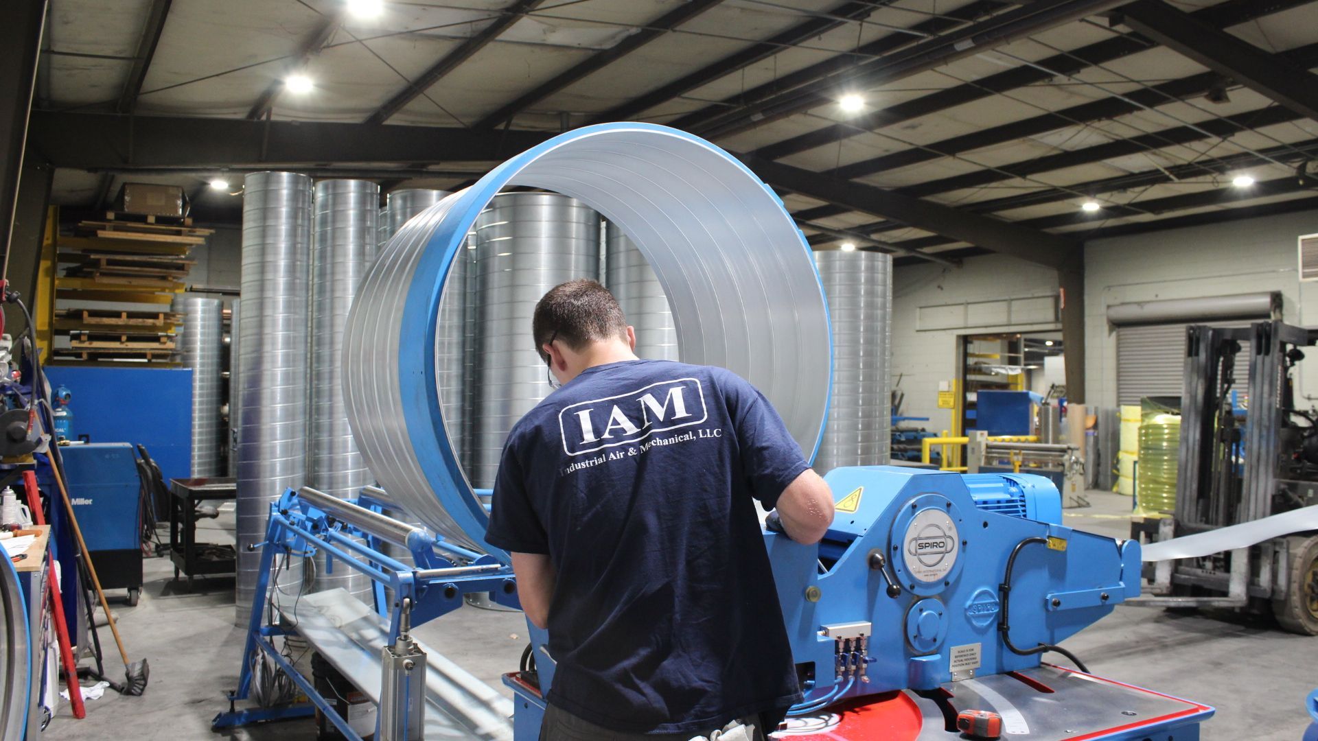 Man in blue shirt works with large metal cylinder in a factory.