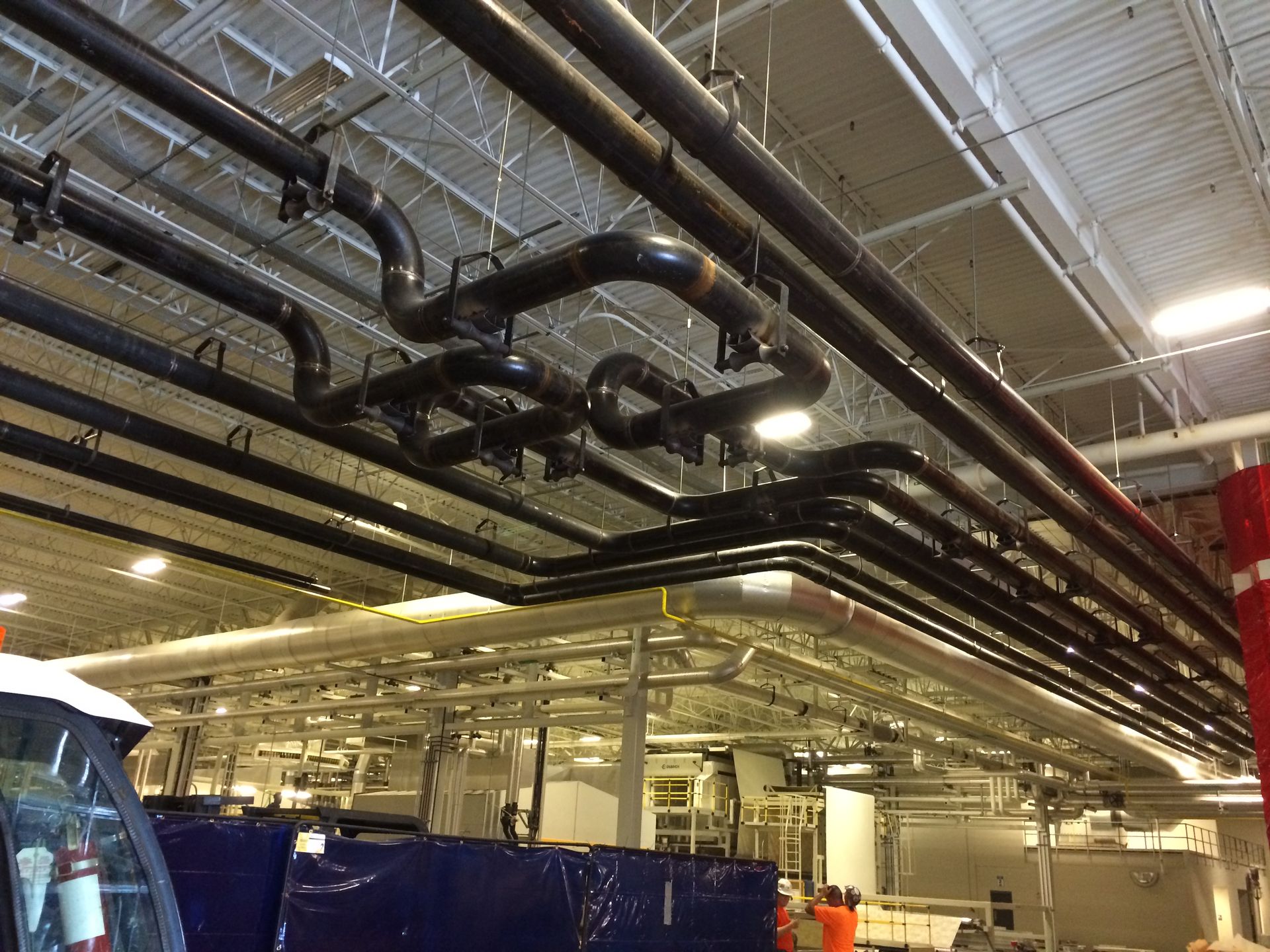 Black pipes and ducts suspended from a white ceiling in a commercial or industrial space.