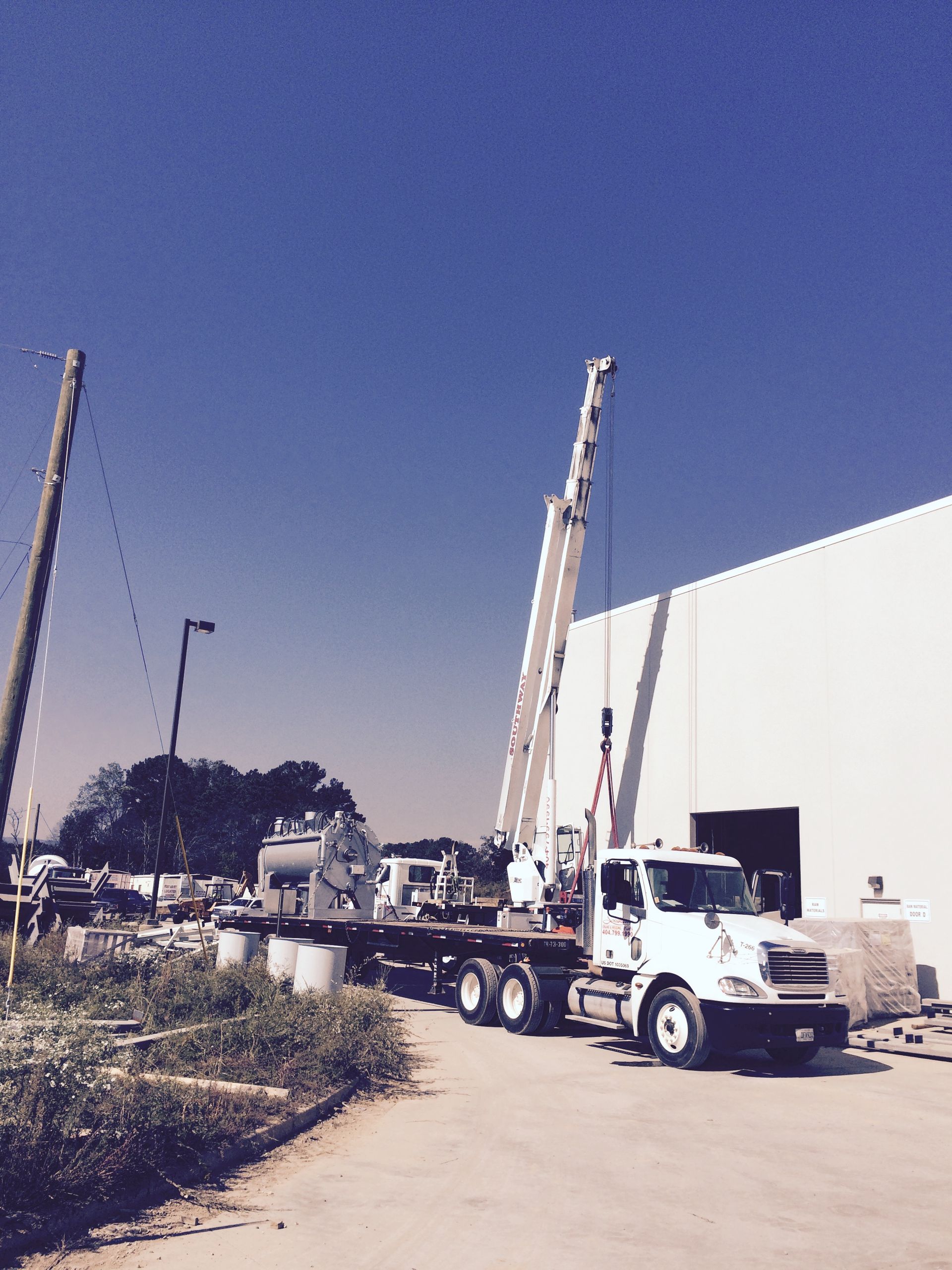A large crane on a truck next to a white building under a blue sky.