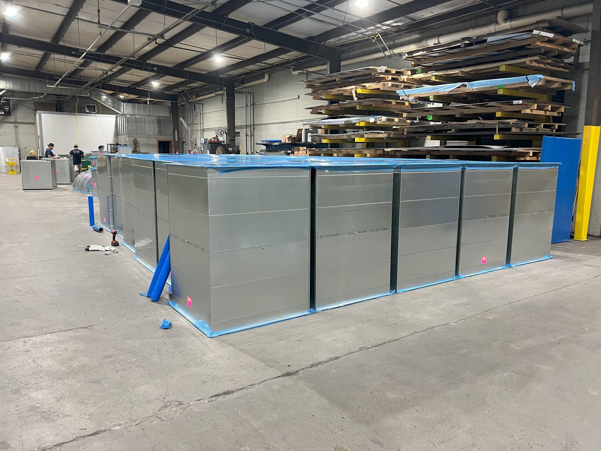 Metal rectangular containers in an industrial setting, wrapped in blue plastic.