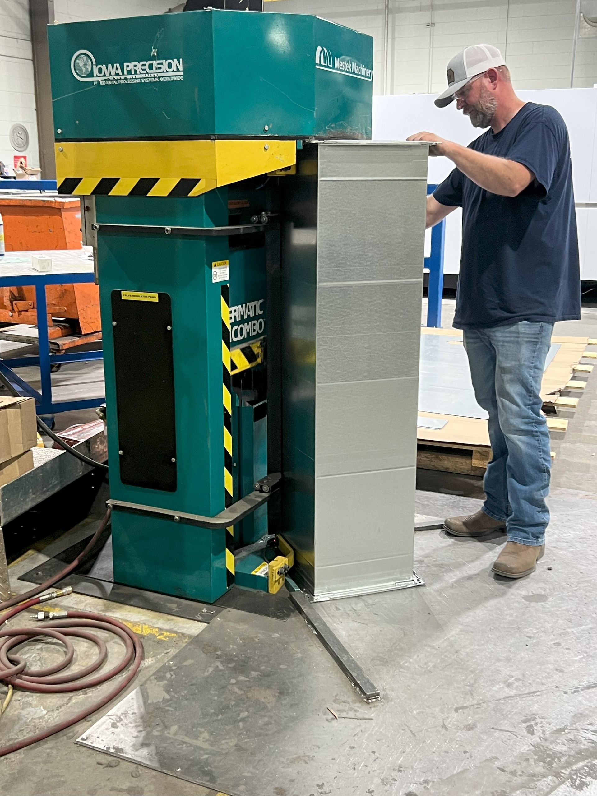 Man using industrial machine to shape a metal duct in a factory.