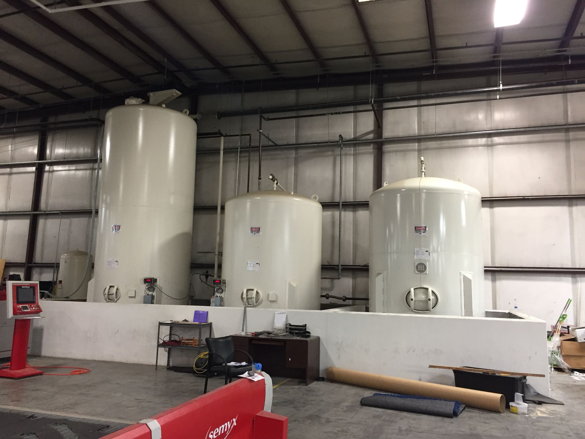 Three large white tanks in an industrial warehouse setting. Plumbing and controls visible.