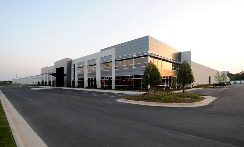 Modern industrial building with gray and silver facade, large windows, and asphalt parking area.