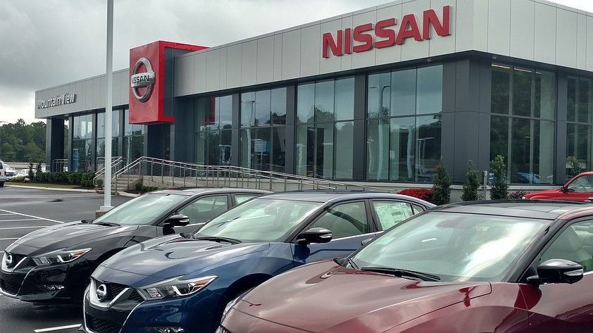Nissan car dealership with cars parked out front, building features large windows and red logo.