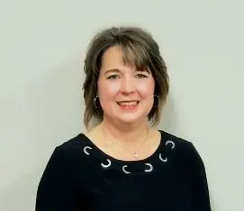 Woman in black top with silver eyelet detail smiles in front of a neutral background.