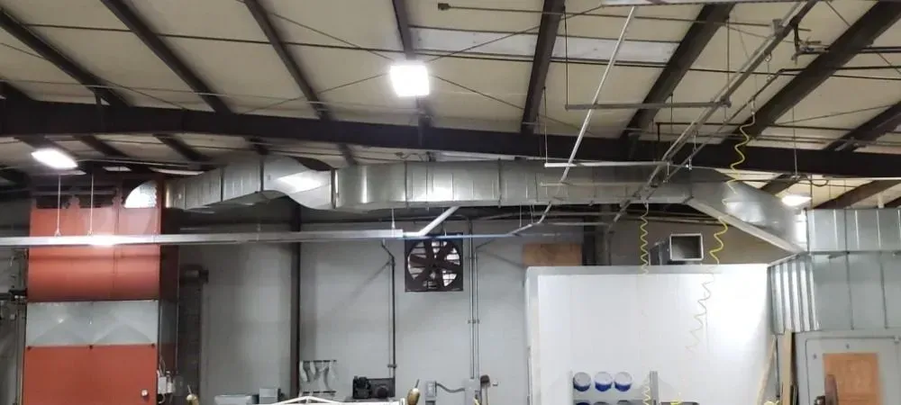 Interior of a large industrial warehouse with exposed ceiling beams, ductwork, and ventilation equipment.