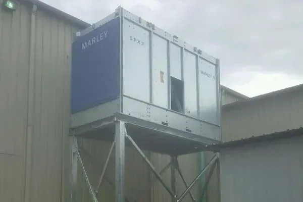 Cooling tower unit mounted on a metal platform attached to a building's exterior. Blue and silver panels.