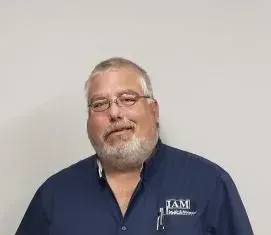 Man with glasses and beard, wearing a blue shirt with a logo, smiling, indoors.