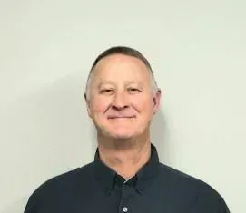 Man in a dark blue collared shirt smiles at the camera against a plain white background.