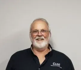 Man with glasses and white beard smiles, wearing a black shirt with 