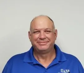 Bald man in a blue polo shirt smiles at the camera against a plain white background.