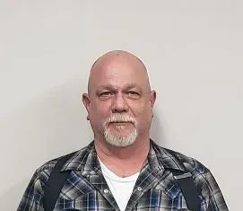 Man with a bald head and goatee, wearing a plaid shirt and white undershirt.