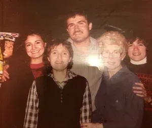 Group of six people smiling, posing for photo. Two women in front, others behind.