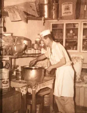Baker mixing ingredients in a kitchen, wearing a uniform, sepia tone.