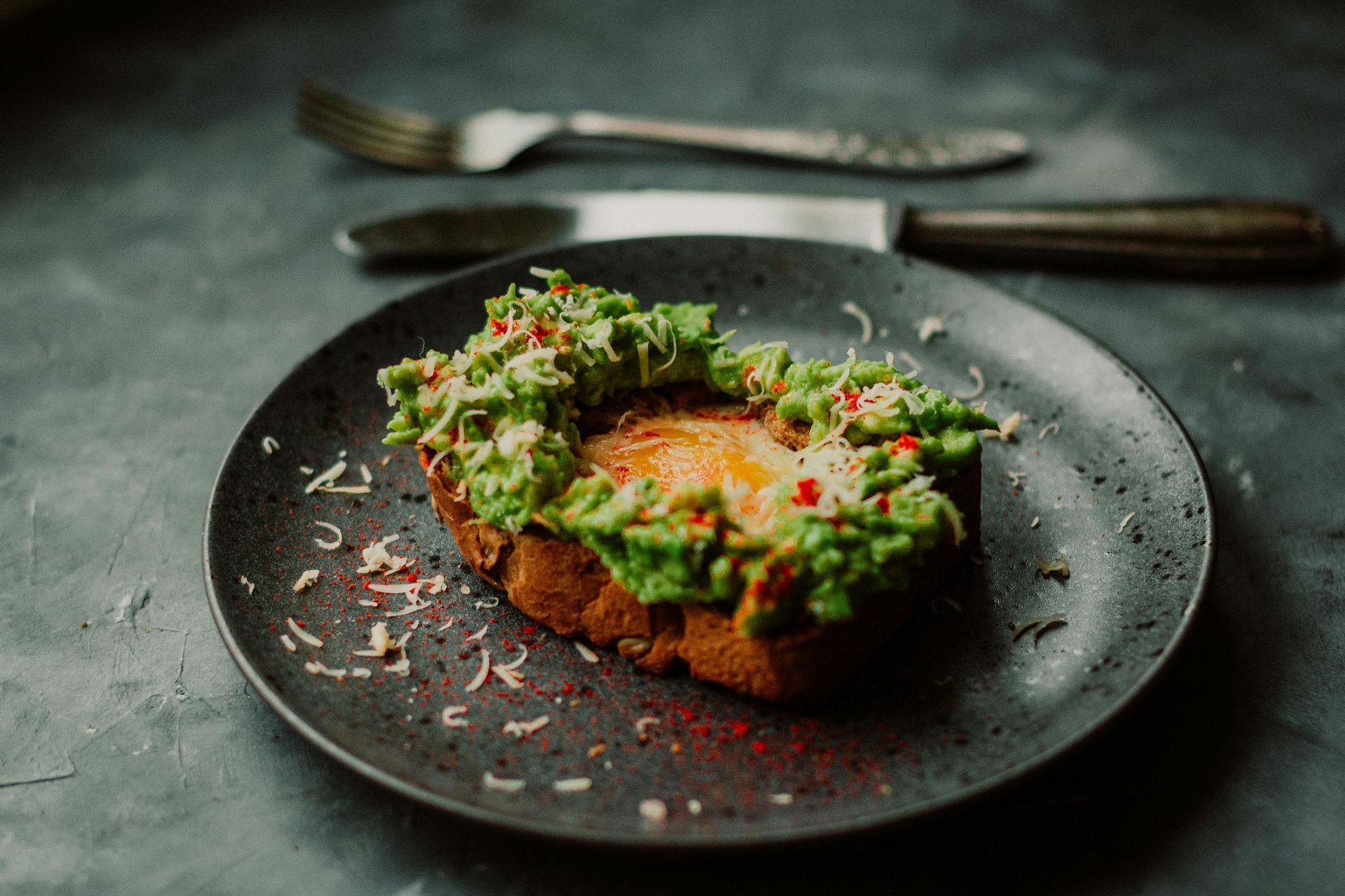 Avocado toast on a gray plate, with a fork and knife in the background.