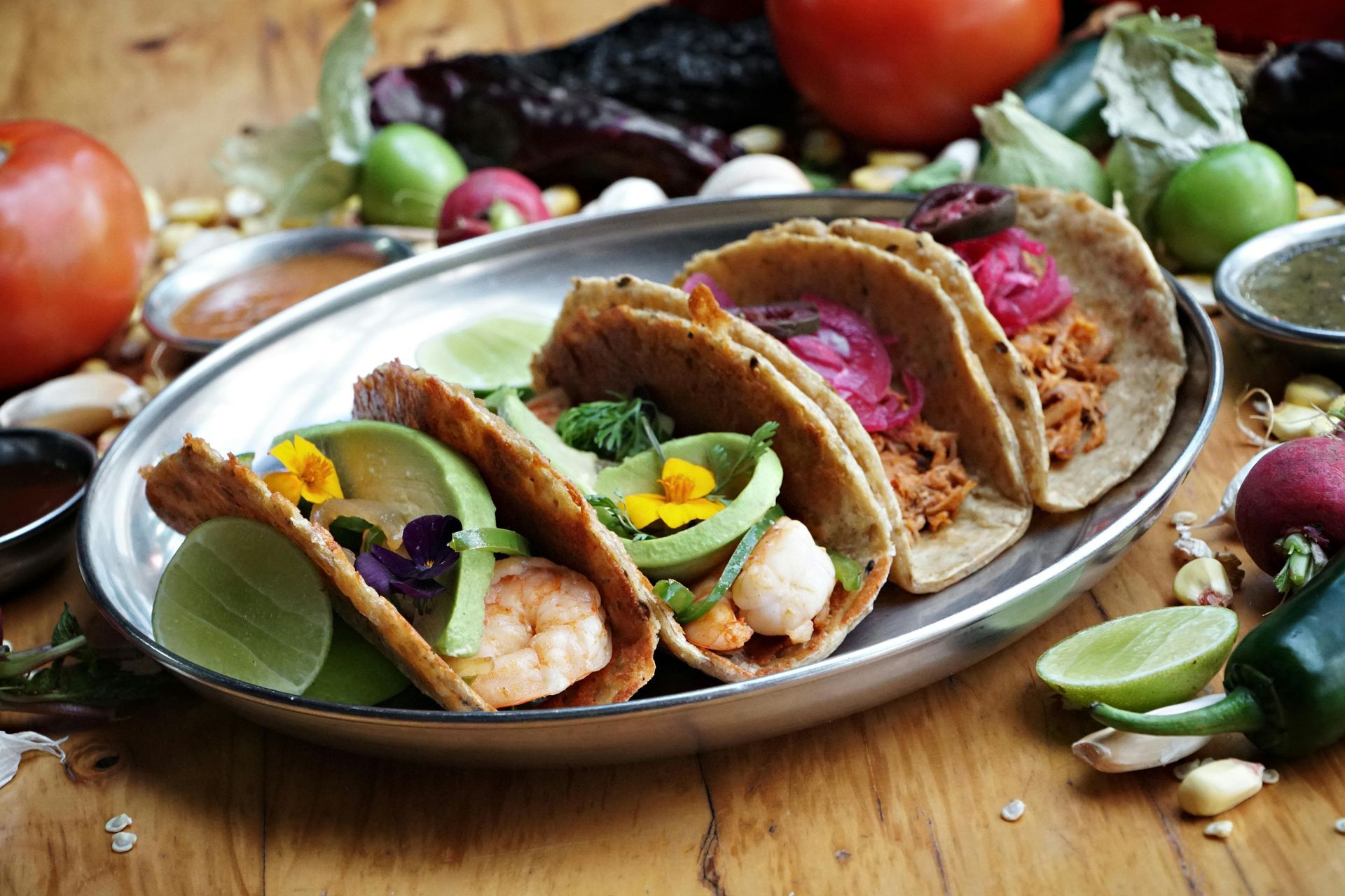 Tacos on a silver platter, various fillings, garnishes, and sides. Wooden table setting.