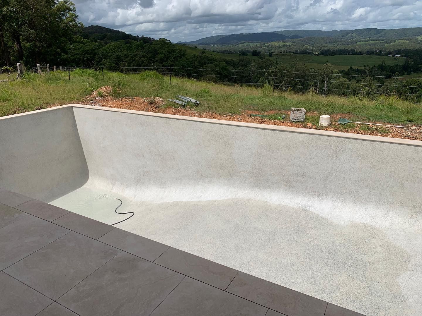 Empty rectangular pool with gray interior, overlooking a green landscape under a cloudy sky. — HinterCoast Pools In Wolvi, QLD