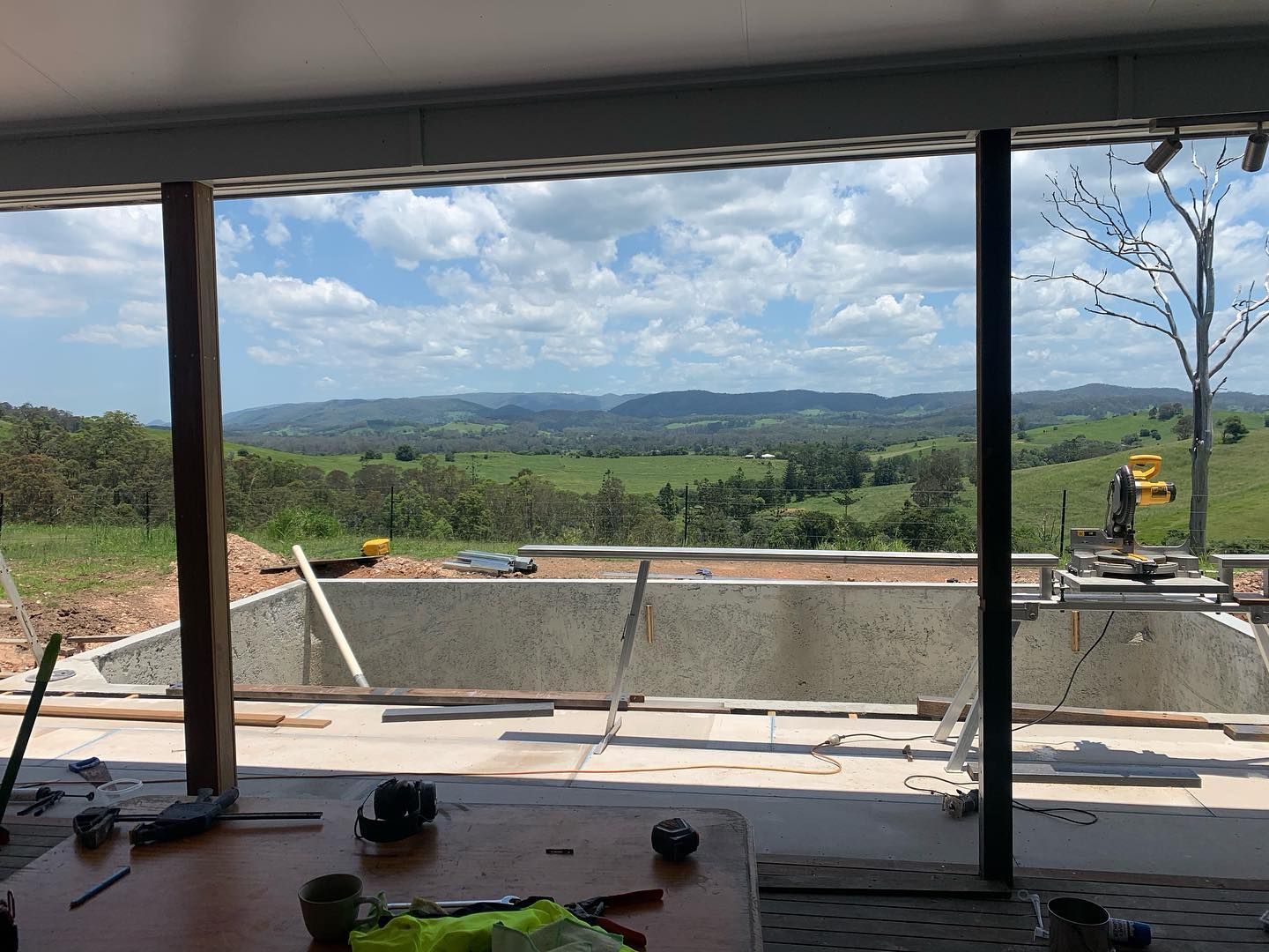 Construction site with valley view framed by dark beams and a window. Cloudy sky. — HinterCoast Pools In Cooroy, QLD
